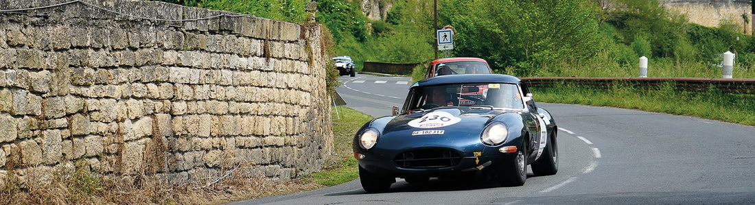 A vintage Jaguar car on a road with a brick wall to the left