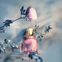 Elegant pink Creed perfume bottle surrounded by delicate pink flowers and soft lighting