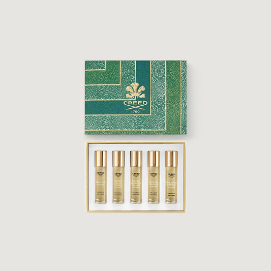 Set of five gold bottles with a green Creed box on a light gray background