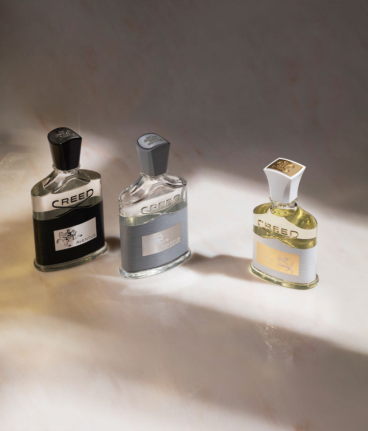 Aventus 100ml bottle, Aventus Cologne 100ml bottle, and Aventus for Her 75ml bottle on a white marble table top