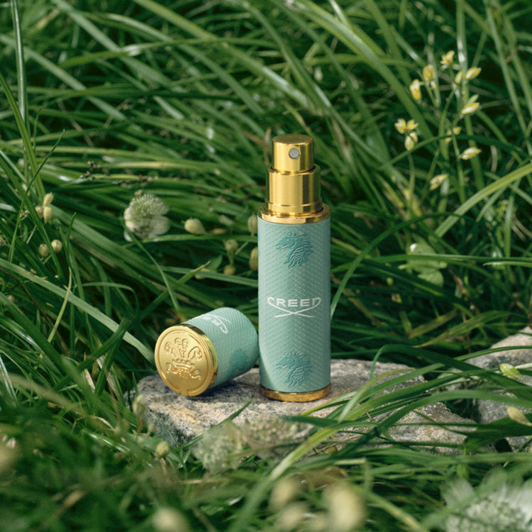 Two Creed perfume bottles on a stone surface with grass in the background