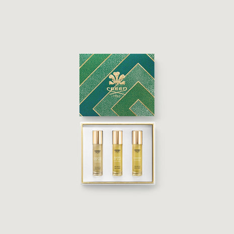 Three Creed perfume bottles in a gold and green box on a grey background