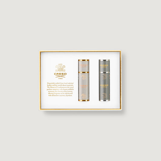 Two atomizers of Creed perfume in a gold-framed box on a light gray background