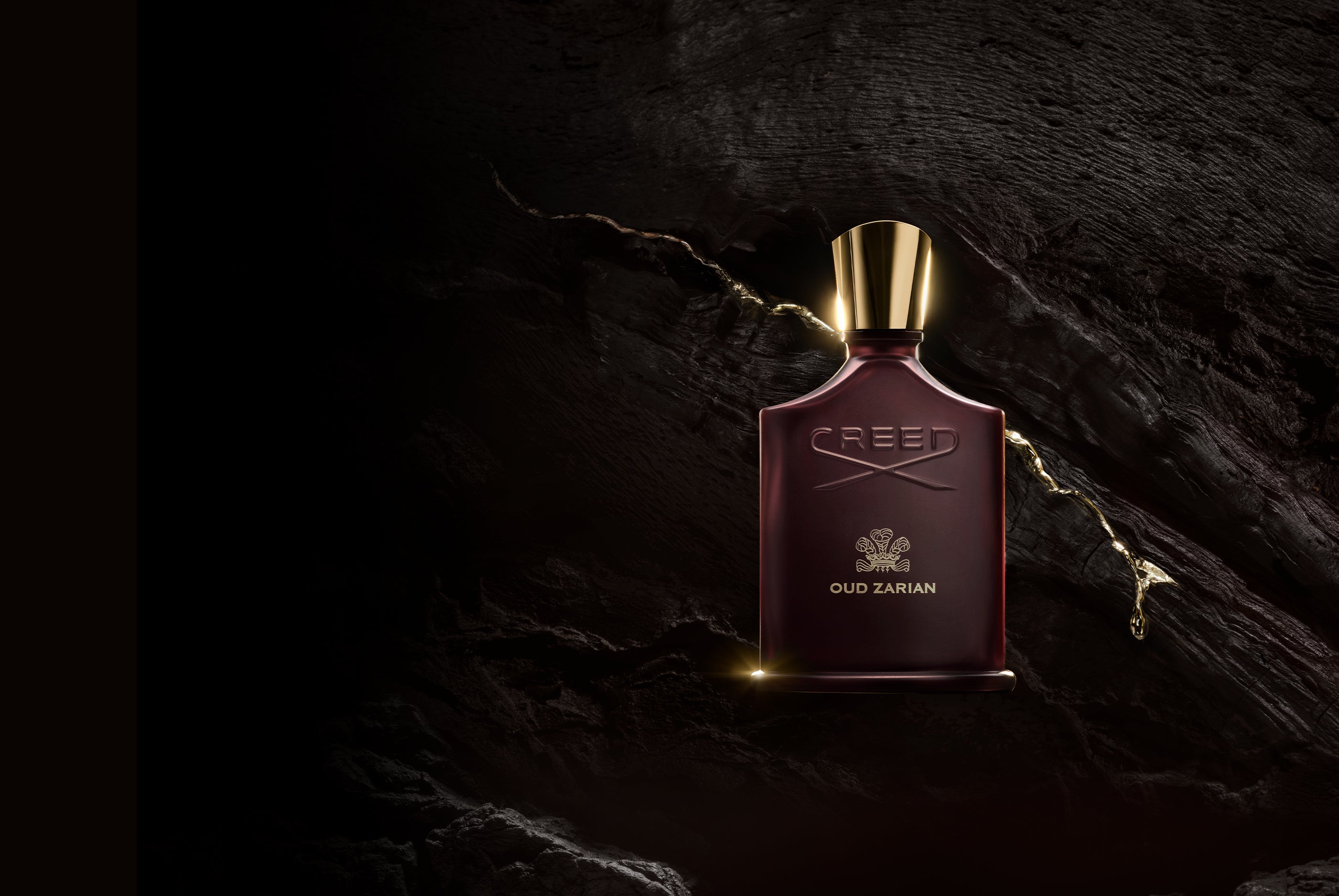 Red Creed perfume bottle with gold cap on a dark stone background
