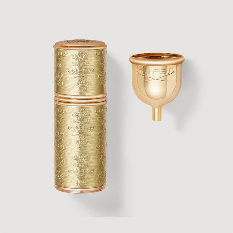A gold-colored, refillable travel perfume atomizer with an engraved design, displayed next to its cap.