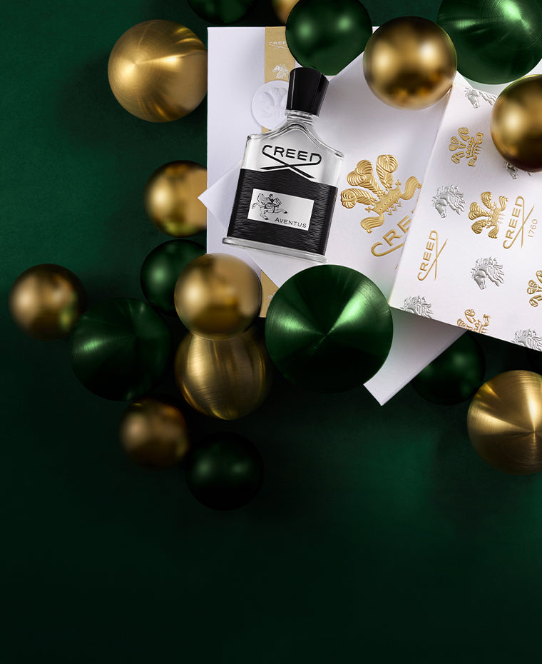 Aventus Bottle is on top of Creed Signature Gift Box featuring Discovery Set, Gold and Green Ornaments around.