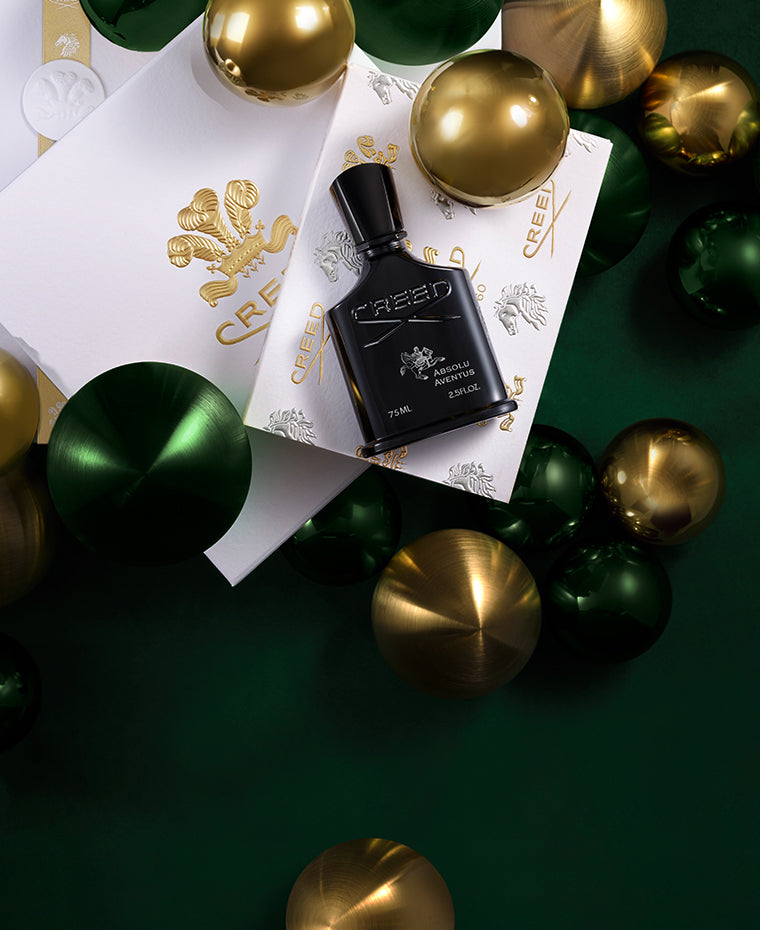 Absolut Aventus bottle is on top of the Creed signature gift box surrounded by gold and green ornaments. 