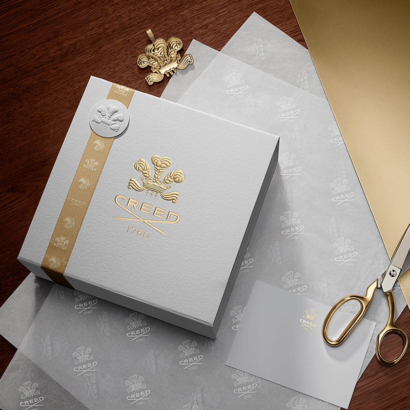Creed branded box and papers on a wooden surface with gold scissors.