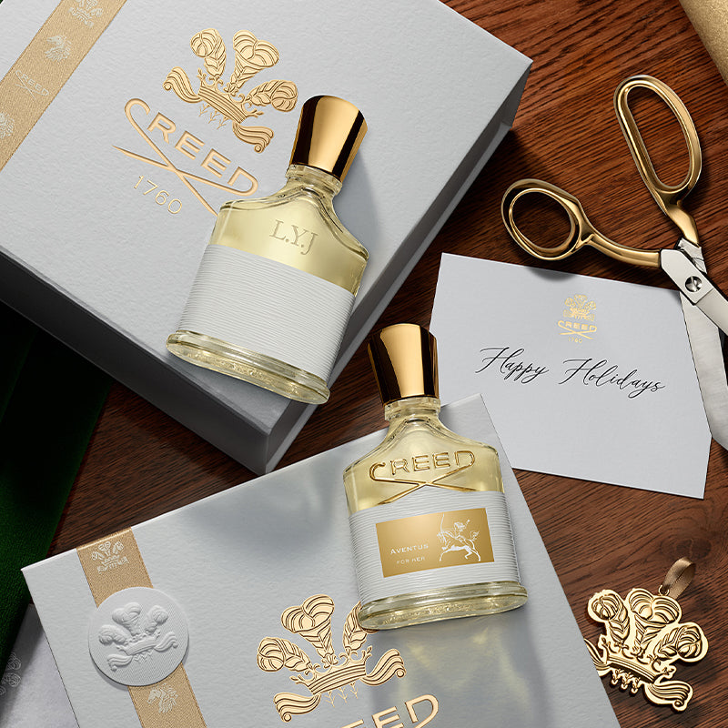 Two Creed perfume bottles with packaging and a card on a wooden surface.