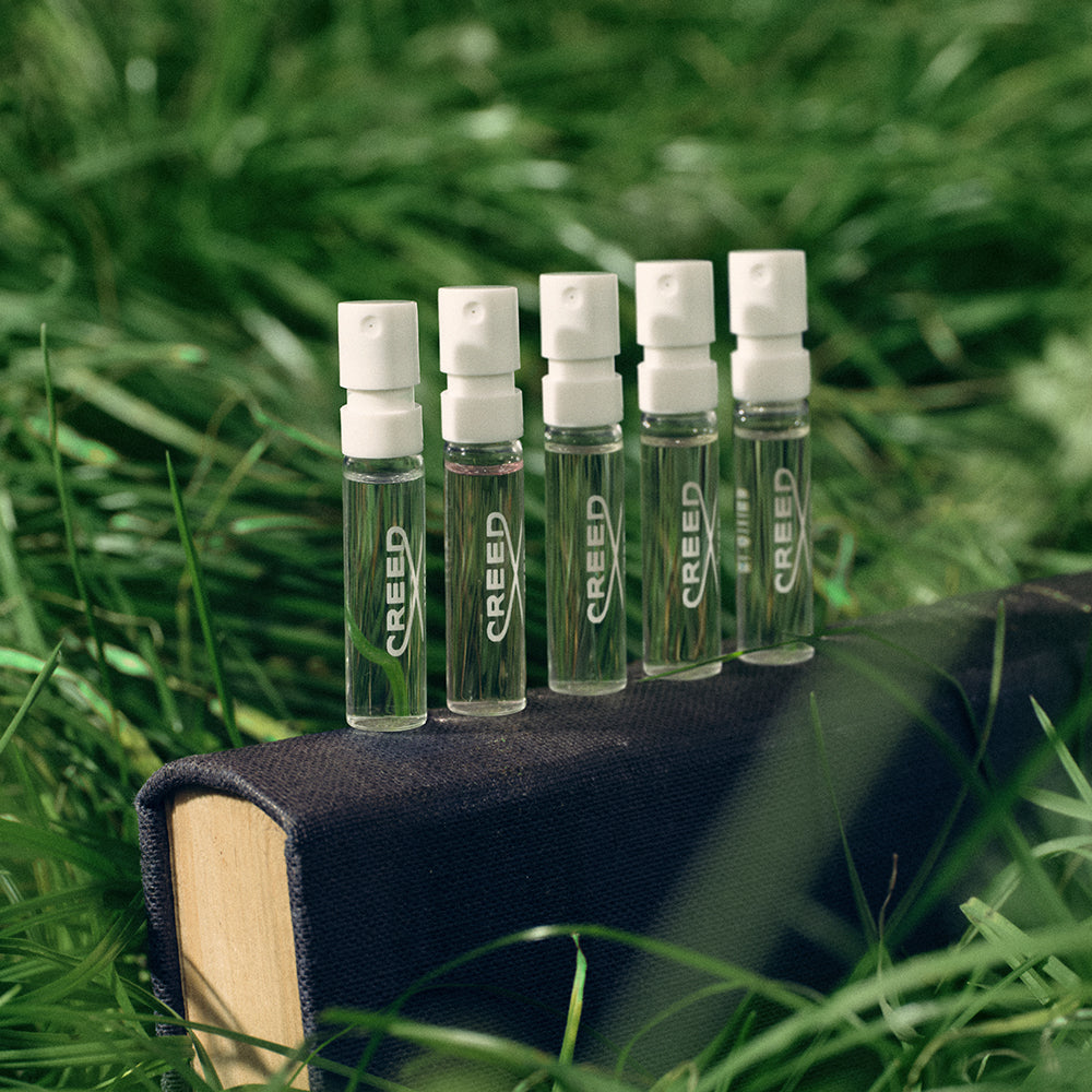 Set of Creed perfume samples on a book with a grassy background