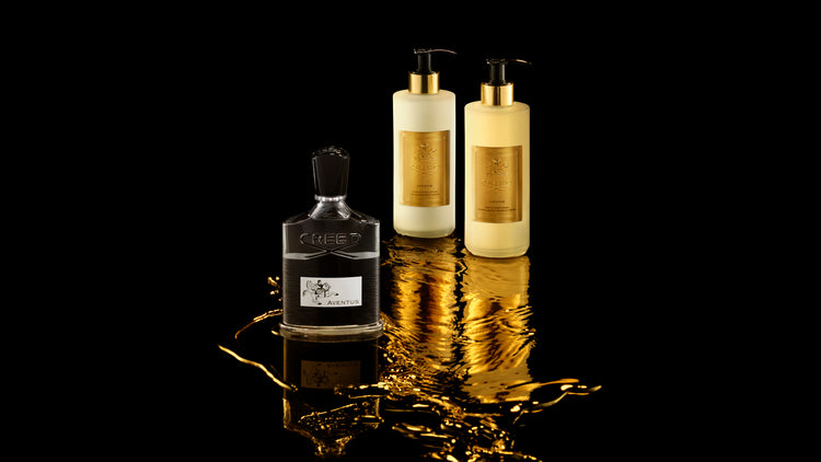 Three bottles of perfume on a reflective black surface with a gold sheen.