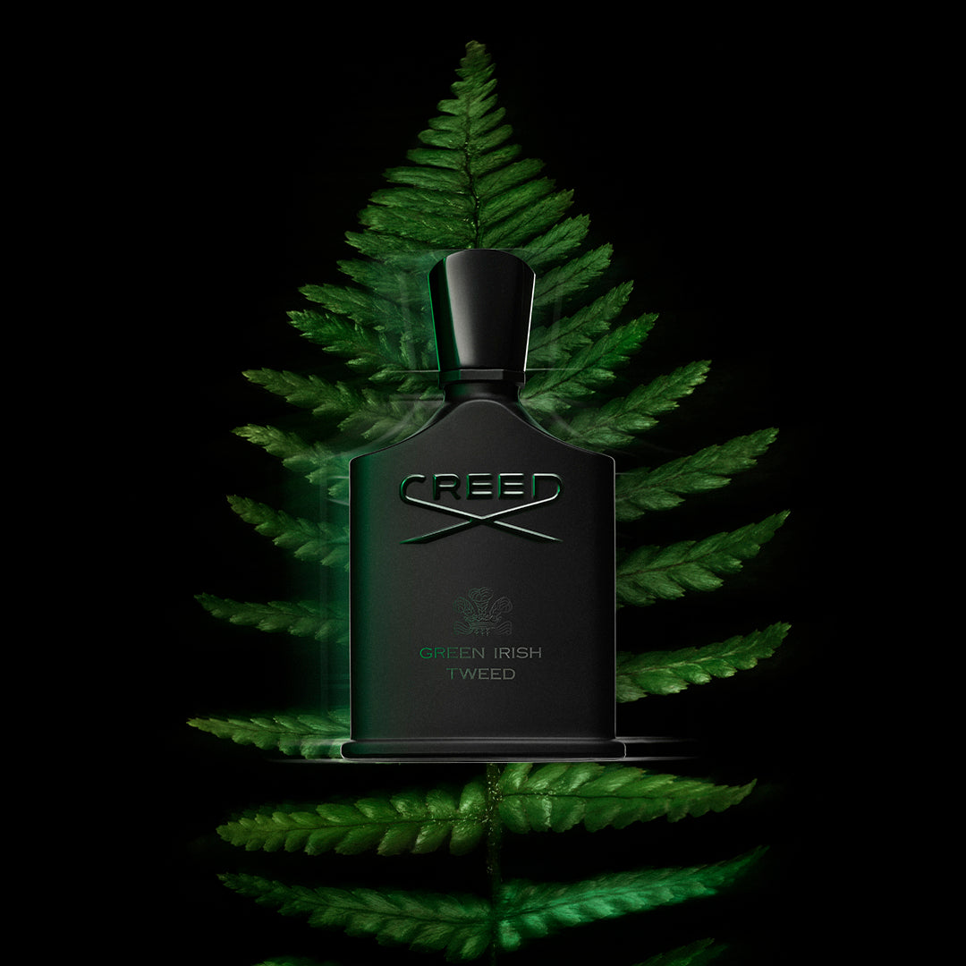 Green Irish Tweed fragrance bottle by Creed surrounded by glowing green fern leaves