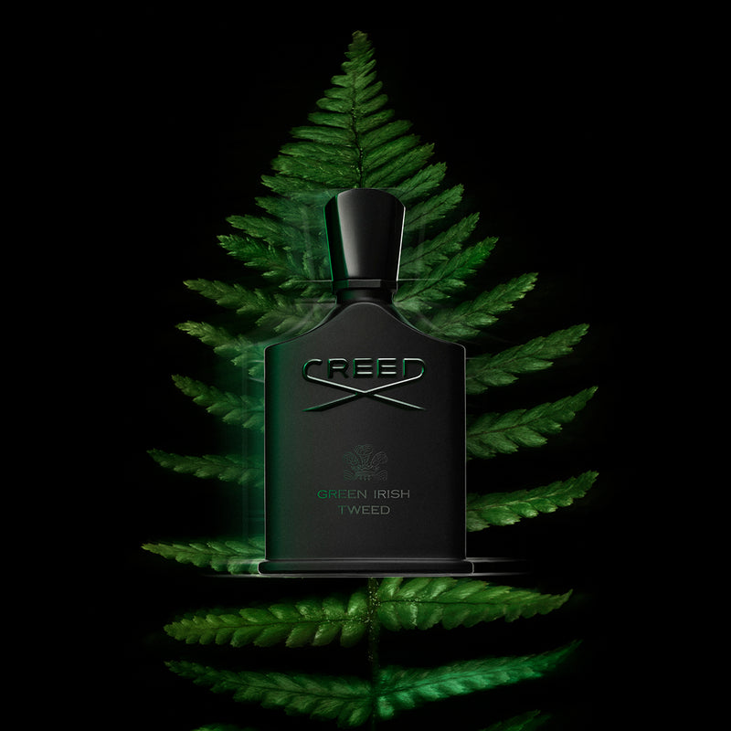 Green Irish Tweed fragrance bottle by Creed surrounded by glowing green fern leaves