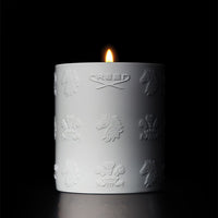 White Creed Boutique candle with embossed logo patterns, illuminated against a black background.