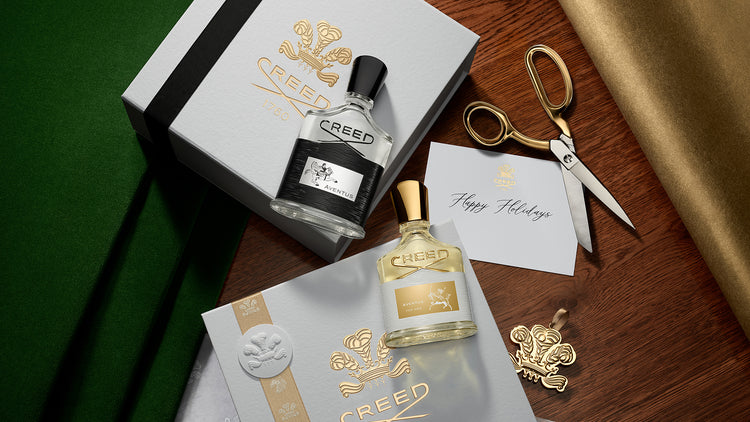 Two bottles of Creed perfume with packaging and a card on a wooden surface.