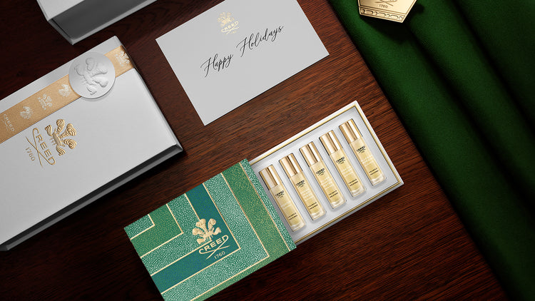 Set of gold bottles in a decorative box on a wooden surface with a 'Happy Holidays' card.