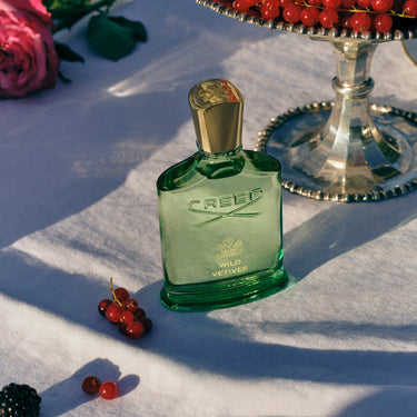 Creed Wild Vetiver perfume bottle on a white tablecloth with berries and flowers.