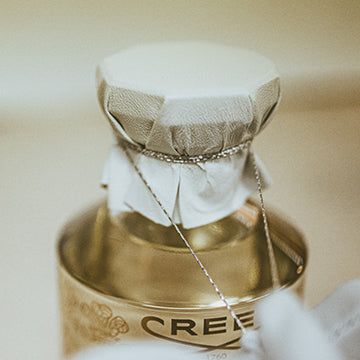 A close-up of a bottle with a gold-toned body and a white fabric-wrapped cap, with part of the word CREE visible on the label.