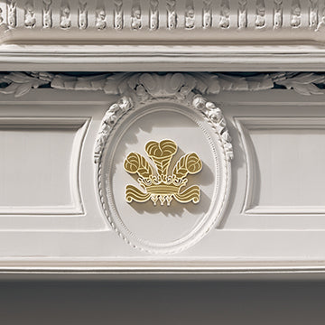 Close-up of an ornate white decorative molding or fireplace mantel detail with a central oval medallion featuring a gold floral emblem.