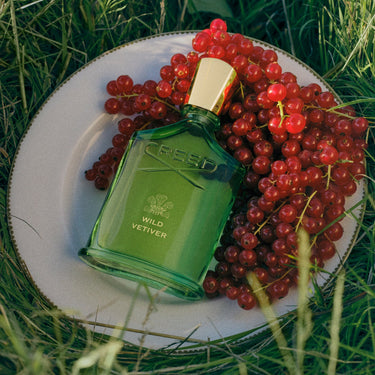 Green Creed perfume bottle on a plate with red berries on a grassy background