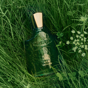 Green bottle of Tree of Life Wild Vetiver perfume on grass with flowers