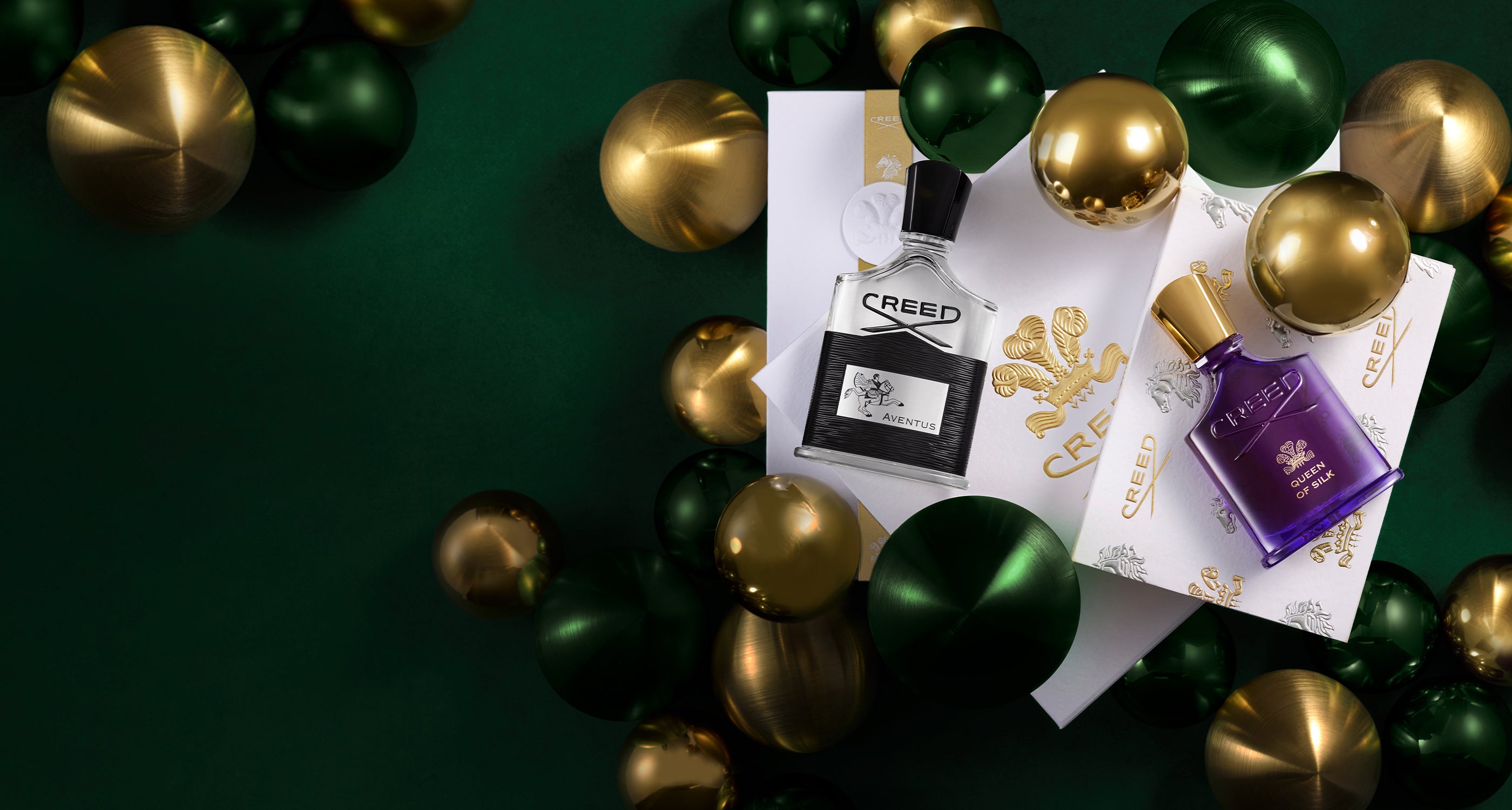 Creed's Aventus and Queen of Silk fragrances, beautifully presented in gift boxes amongst shimmering gold and green ornaments.