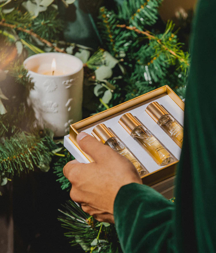 Creed Boutique holiday gift set with Creed perfume bottles, white and gold packaging, and festive green and gold ornaments.